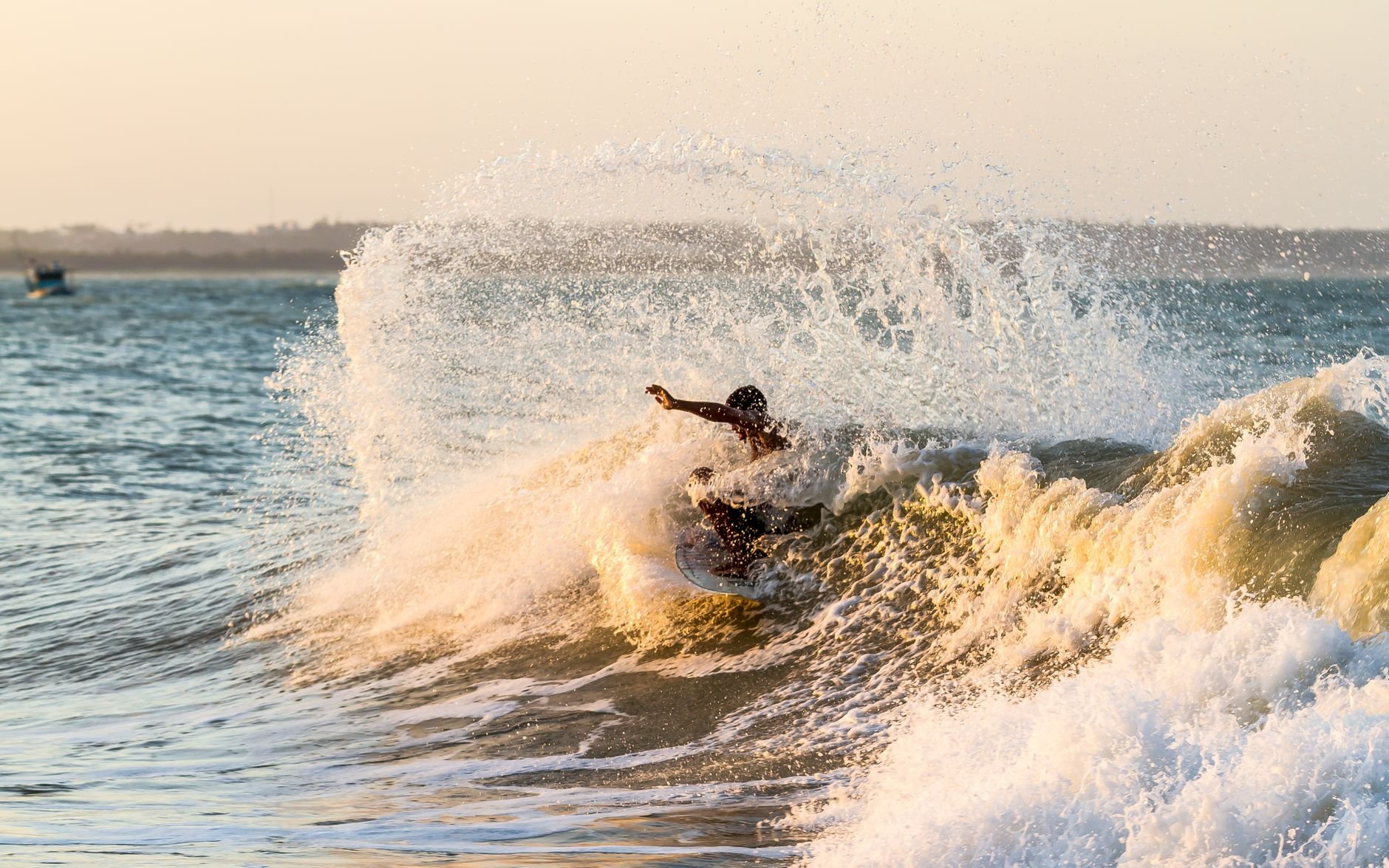 Surfer riding a wave at sunset with dramatic ocean spray, capturing the essence of summer water sports.