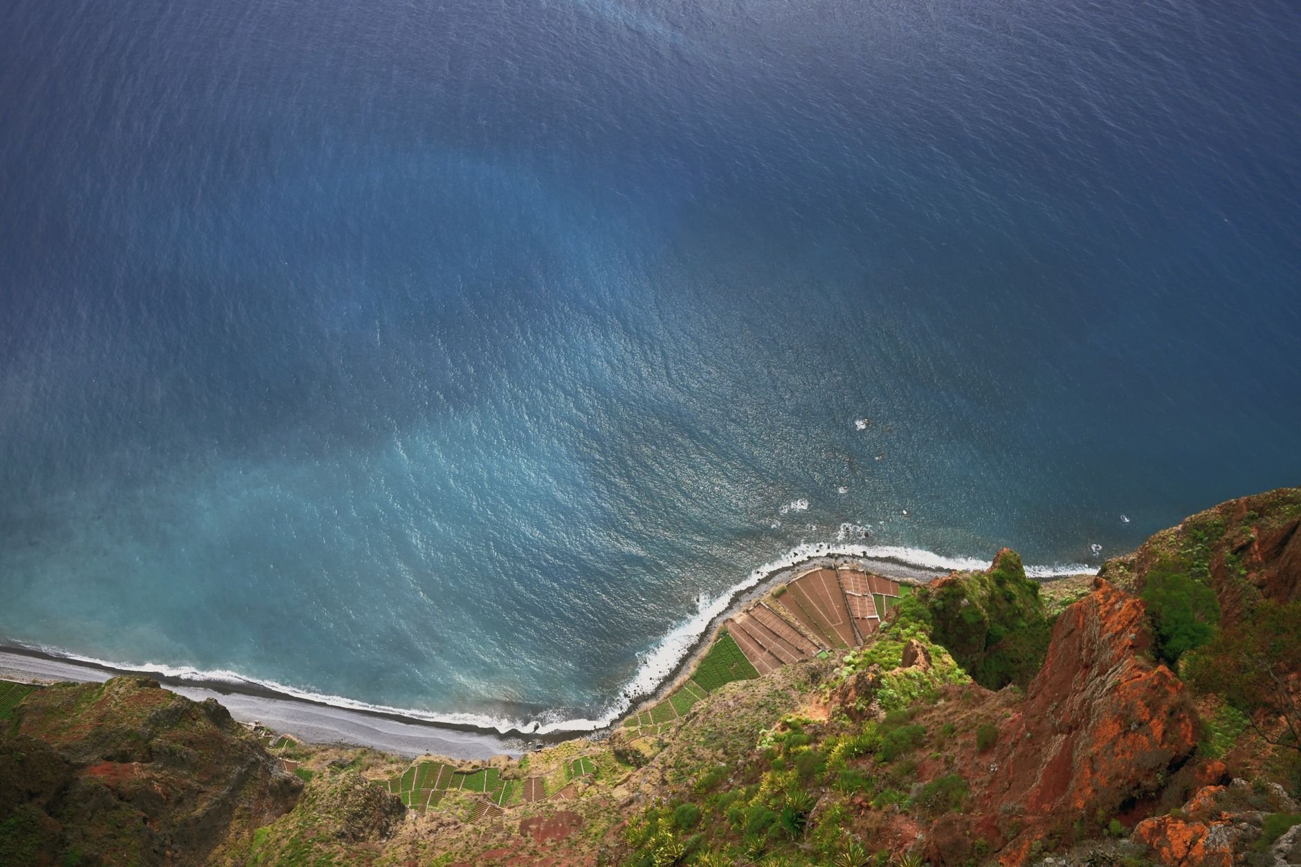 Aerial view of dramatic cliffs with lush greenery meeting the ocean waves.